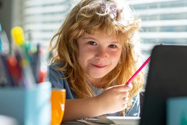 Портрет школяра, який сидить на столі, робить домашнє завдання. Дитина тримає олівець і пише. Хлопчик малює на білому папері за столом. Початкова школа та концепція домашнього навчання . — стокове фото