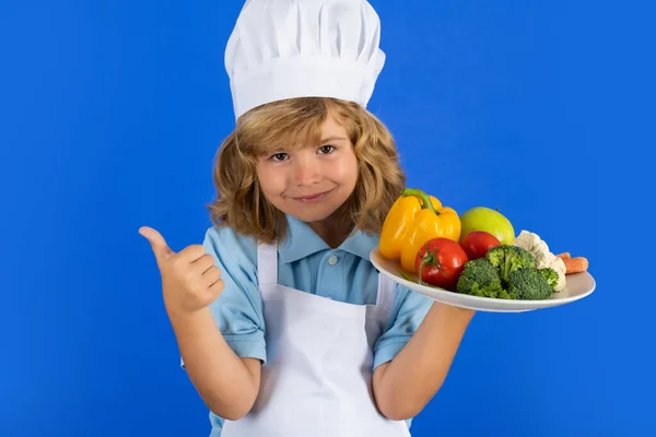Aşçı önlüğü giymiş çocuk aşçı ve stüdyo arka planında izole edilmiş sebze tabağı. Sağlıklı beslenme çocuklar için.. — Stok fotoğraf