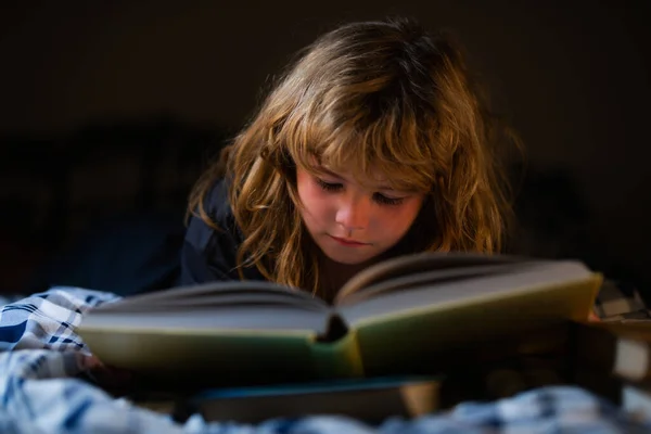 En liten söt pojke som läser en bok som ligger på sängen. Begreppet utbildning och läsning. — Stockfoto