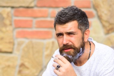 Sigara içen adam. Sakallı adam tuğla duvara karşı sigara içiyor. Sigara bağımlılığı.