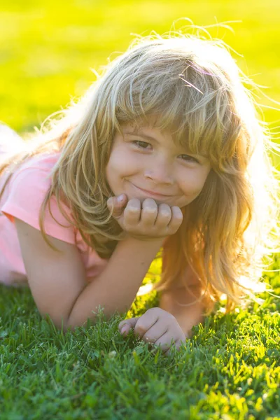 Cara de niño de verano. Niño sonriente con fondo de hierba. Niño en el parque al aire libre. Chico de primavera acostado en la hierba. Caminata de verano. Cálido día de verano durante las vacaciones escolares. Niño niño soñando y sonriendo. — Foto de Stock