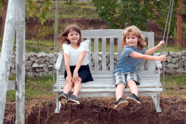 夏の公園で2人の子供が屋外でスイングしてリラックスします 兄と妹の自然の中で幸せな歩行 兄弟男の子と女の子遊びで庭 — ストック写真