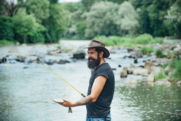 若い髭を生やした男が湖や川で釣りをしている フライフィッシング ヒッパー髭の男がマス魚を捕まえる — ストック写真