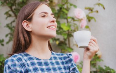 Çekici kadın kahve ile poz veriyor. Neşeli gülümseyen kız kahve içer, baharda arka planda