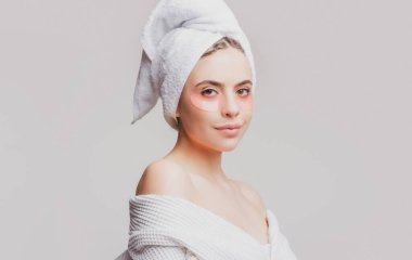 Göz bantlı güzel kadın mükemmel bir cilt etkisi gösteriyor. Gri stüdyoya izole edilmiş yüz bantlarına başvuran çekici genç bir kadının portresi.