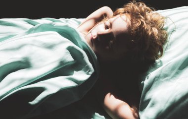 Sakin bir çocuk rahat bir yatakta uyur yumuşak bir yastıkta yatar ortopedik yatakta, güzel bir çocuk battaniyeye sarınır yatak odasında, üst manzara