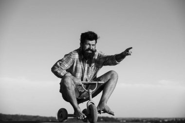 Küçük bir bisiklet süren çılgın bir adam. Sakallı bir adamın, dışarıda bisikletle eğlenen çılgın bir hippi portresi.