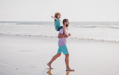 Baba ve oğul denizde yürüyor. Yakışıklı adam baba, küçük oğlan çocuğu taşıyor. Mutlu baba kucağında çocuğu. Babacığın küçük oğluyla yaz günü. Arkadaş canlısı aile kavramı ve yaz tatili