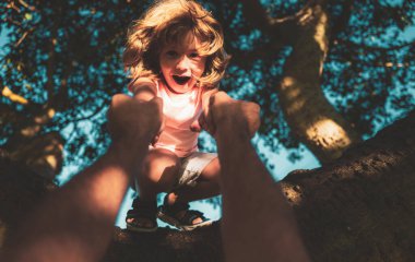 Baba oğlunun ağaca tırmanmasına yardım ediyor. Ağaca tırmanan tatlı çocuk. Ebeveyn, çocuğun elini tutar.