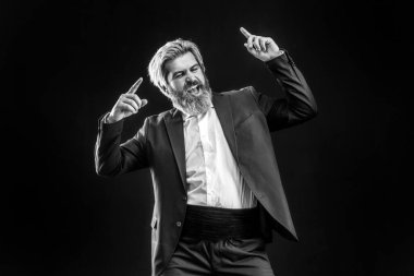 Siyah takım elbiseli, kulaklıklı, gri arka planda dans eden mutlu genç iş adamı.