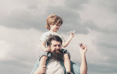 Babalar günün kutlu olsun. Baba ve oğul arka planda oynuyorlar. Baba ve oğul parkta. Hayal Özgürlüğü - Neşeli Çocuk Kağıt Uçakla Oynuyor