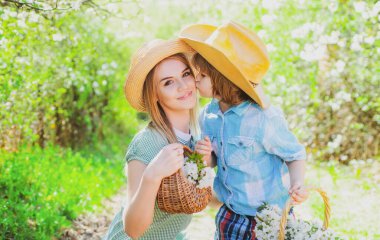 Çiçekli kır çiçekleriyle dolu sepeti olan mutlu bir anne ve oğlu var. Parkta çimlerin üzerinde oturan çocuklu bir anne.