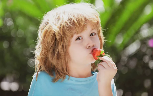 幸せな男の子は緑の夏の背景にイチゴを食べる — ストック写真