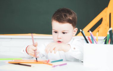 Çocuk sınıfta yazı yazıyor. Öğrenci çocuk evde ders çalışırken ödev yapıyor.