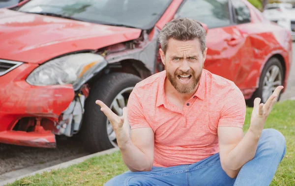Stressed driver sitting on the road next to broken car