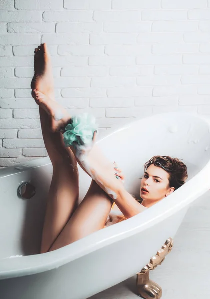 浴槽にスポンジで彼女の足をマッサージバスルームで女性 足を浴槽で洗う女 若い女性のショットがバスタブに横たわって離れて見て — ストック写真
