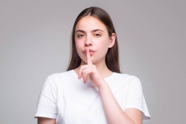Şşş, kadınların sırları. Gizli işaret gösteren bir kadın. Ağzında parmak olan bir kadın. Genç bir kadının yakın plan portresi 