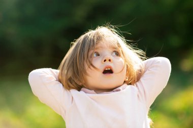 Baharda yeşil çimlerde gezen süpriz kız çocuğu. Parkta yürüyen küçük çocuklar. Duygusal bebek yüzü