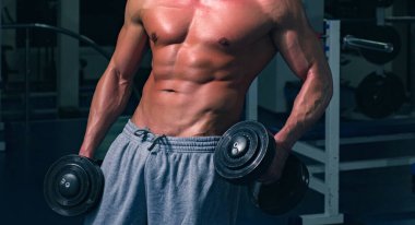 Çıplak karın kasları. Spor salonundaki sporcu. Çıplak gövdeli sportif bir erkek. Antrenman adamı. Dambıllı egzersizler. Güçlü atletik vücut