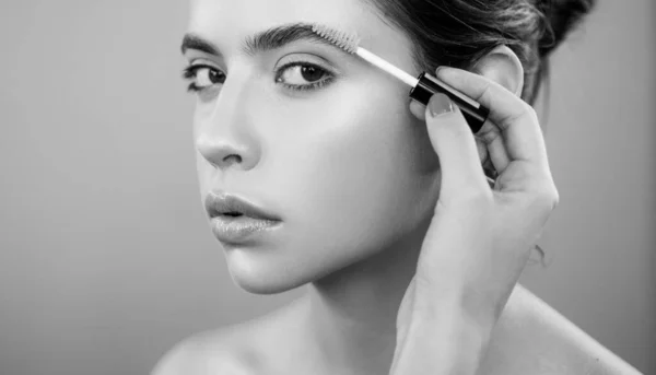 Care beauty eyebrow. Beautiful woman with brow brush in hand. Attractive sexy girl with glamorous professional nude makeup brushing up her perfect eyebrows with brush. Natural eyebrow makeup look