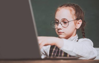 Masada oturan ve deftere yazan küçük bir öğrenci. Elinde kitap olan bir çocuk. Kapatın. Çocuk arkaplanda bir tahtayla cevap vermeye hazır.