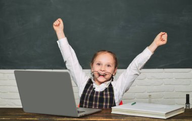 Laptop ile küçük öğrenci öğrencisi. Öğrenci tahta arka plan üzerinde dizüstü bilgisayar üzerinde çalışıyor. Okul sınıfında kara tahta yakın çocuk. Çocuk tahta arka planda sınıfta öğreniyor
