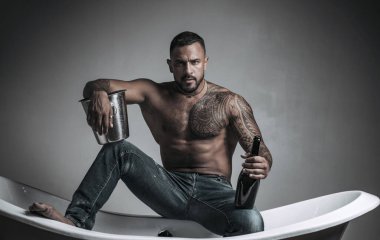 Şampanya kutlaması. Gri arka planda dövmeli yakışıklı bir adam. Seksi gece partisi, genç aşıklar. Kot pantolonlu moda adamı bacakları