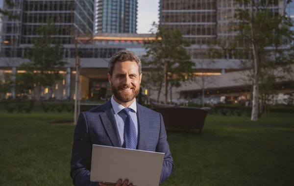 Businessman with notebook outdoor. Confident business expert. Handsome man in suit holding laptop against office background