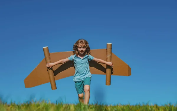 青い空に対しておもちゃの飛行機の段ボールの翼で幸せな子供の遊び 夏の野外で楽しんでいる子供 紙翼を持つ少年の肖像 — ストック写真