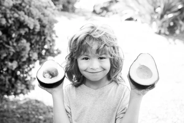夏の庭でアボカドを見せてくれる幸せな子供 子供の健康食品 — ストック写真