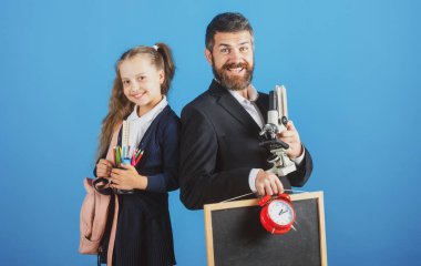 Öğretmen ve öğrenci kız okula hazır. Mavi arka planda izole edilmiş okul malzemeleriyle baba ve küçük kızların portresi.