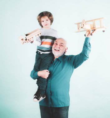 Gelecek nesil aile rüyası. Mavi arka planda oyuncak uçağı olan mutlu büyükbaba ve torun izole edildi. Mutlu büyükbaba, torununu sırtında taşıyor.