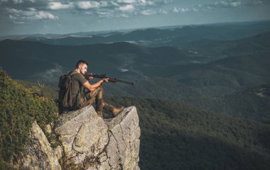 Yakışıklı avcı adam silah tutuyor ve ormanda yürüyor. Silahlı bir erkek. Av dönemi yaz sezonu. İzini sür. Dağ avı. Avdan sonra av tüfeği tabancalı avcı