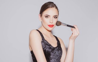 Güzel esmer genç bir kadın makyaj fırçasıyla yanaklarına pudra sürüyor. Güzel kadın, kadın cilt bakımı, yüz güzelliği portresi