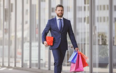 Alışveriş torbaları tutan ve alışveriş mağazasında yürüyen bir iş adamı. Alışveriş ve ödeme. Alışverişkolik alışveriş kavramı