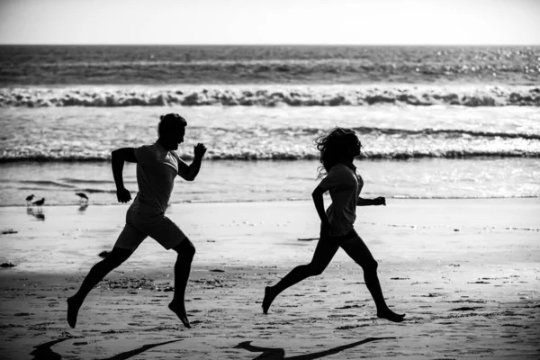 ビーチを走っているカップル スポーツと健康的なライフスタイル ビーチで日没時にジョギングシルエットの友人 — ストック写真