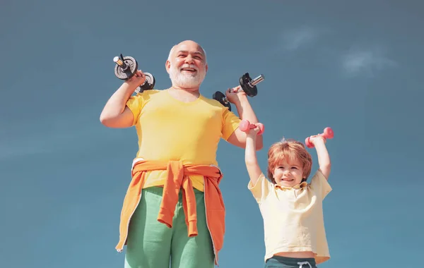 Active family enjoy sport and fitness. Funny old senior man and kid boy with dumbbells. Grandfather and child do morning exercise