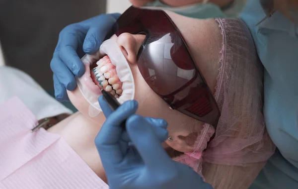 牙医在一个愉快的环境中在牙科诊所治疗一名女病人 年轻的金发碧眼的女性张开嘴 而无法辨认的牙医在乳胶手套检查她的牙齿的条件 — 图库照片