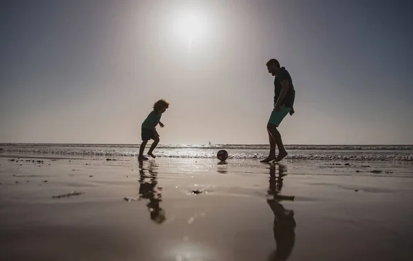 父と息子は夏休みにビーチでサッカーやサッカーをします 夏の日に遊んでいる子供の男の子とパパ — ストック写真