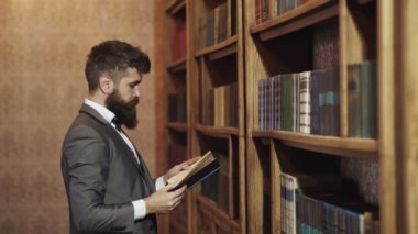 Düşünen adam. Kütüphanede sakallı adam ve arka plan kitapları. Orta yaşlı bir adam kütüphanede kitap okuyor. Kütüphanedeki kendinden emin yetişkin öğrenci.