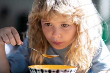 Bulanık arka planda yemek yiyen çocuk. Aç küçük çocuk yemek yiyor. İçeride sebze çorbası içen sevimli küçük okul çocuğu. Çocuklar için ev yemeği
