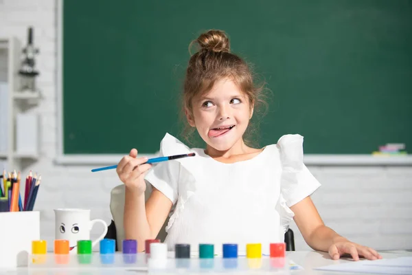 小女孩坐在桌旁 在教室里画画 在黑板上玩得很开心 一点有趣的画家画 绘画艺术 有趣的孩子情绪 — 图库照片