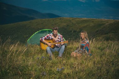 Romantik çift kampta gitar çalar. Doğa dostu arkadaşlarla açık hava macerası. Yaz mevsiminde ormanda kamp yapan çiftler.