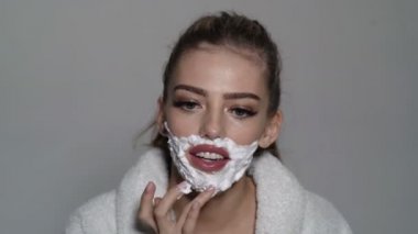 Yüzünde köpük ve jilet olan seksi, şehvetli genç bir kadın. Tıraş olan kadın