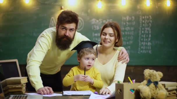 若い家族が勉強する 家庭で遊ぶ家族 両親は家で子供たちの宿題を手伝っている 幼い父と母は息子がリビングルームで勉強するのを助けています — ストック動画