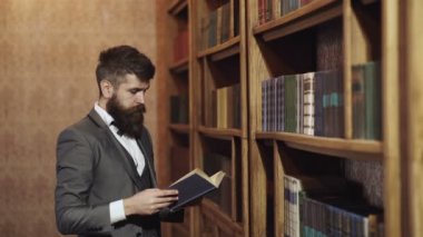 Kitaplık arka planında sakallı, kitap okuyan otantik bir adamın portresi. Klasik takım elbiseli iş adamı kitap okudu. Eski moda iş adamları. Adam kütüphanede kitap seçiyor.