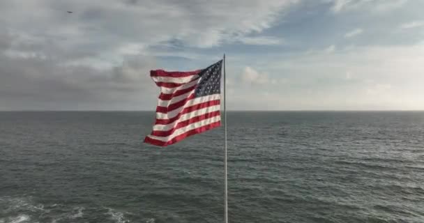 ドローンで飛んで空中からの眺め 海や海の近くの風に吹くアメリカの旗 — ストック動画