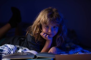 Yatakta uzanmış kitap okuyan sevimli bir çocuk. Hayal gücü ya da öğrenme kavramı