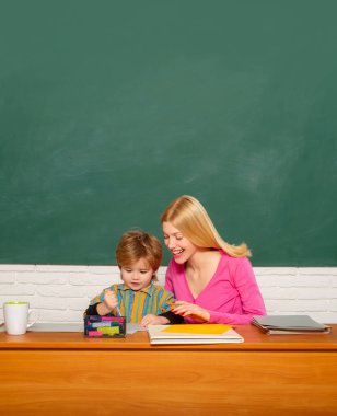 Öğretmen, genç öğrenciye yazı dersinde yardım ediyor. Okul çocukları ve öğretmenleri derste konuşuyor.