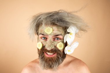 Yüzünde balçık maskesi ve salatalık dilimleri olan komik bir adam.